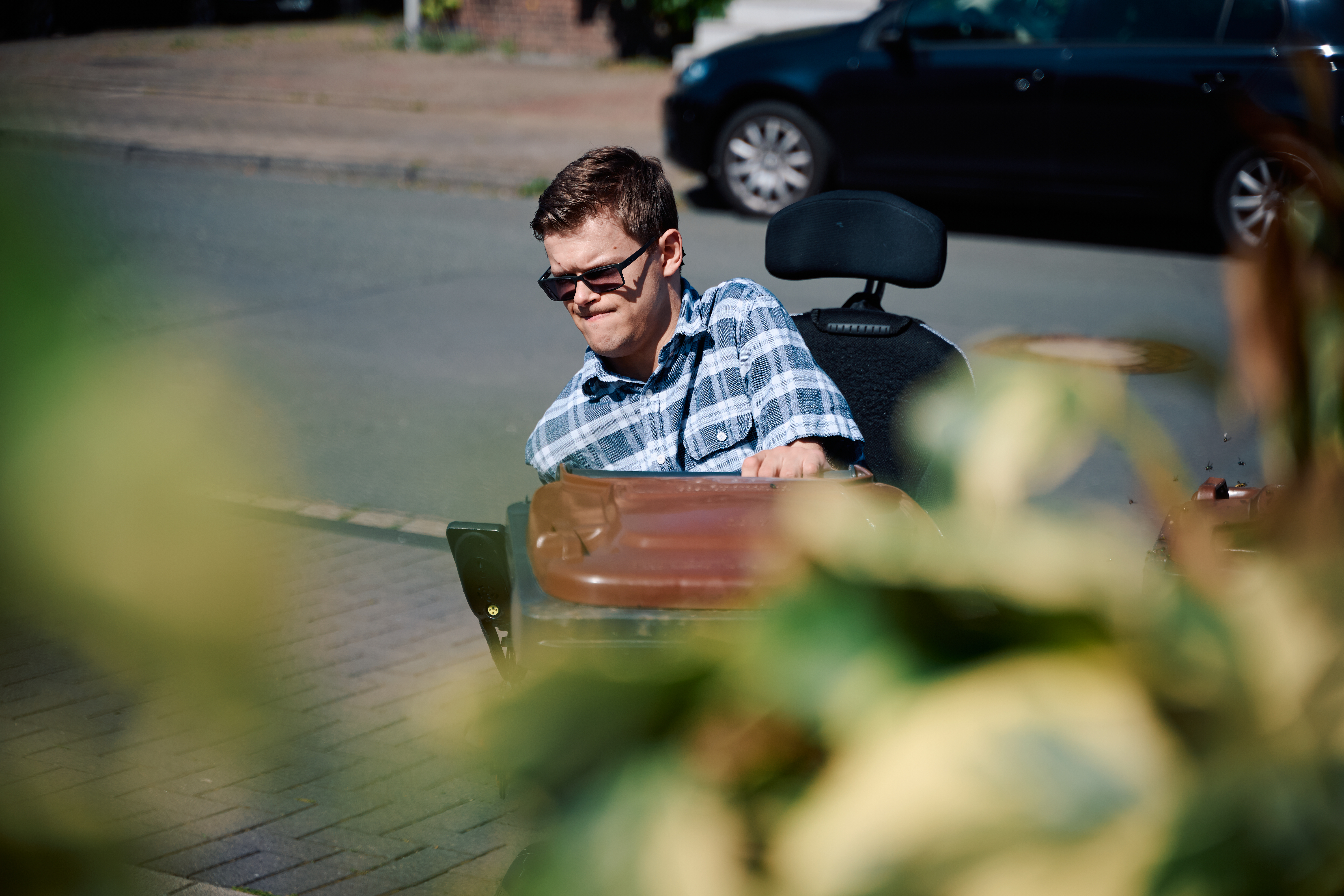 Ein junger Mann mit Sonnenbrille im Rollstuhl zieht eine Bio-Mülltonne. Ein junger Mann mit Sonnenbrille im Rollstuhl zieht eine Bio-Mülltonne.