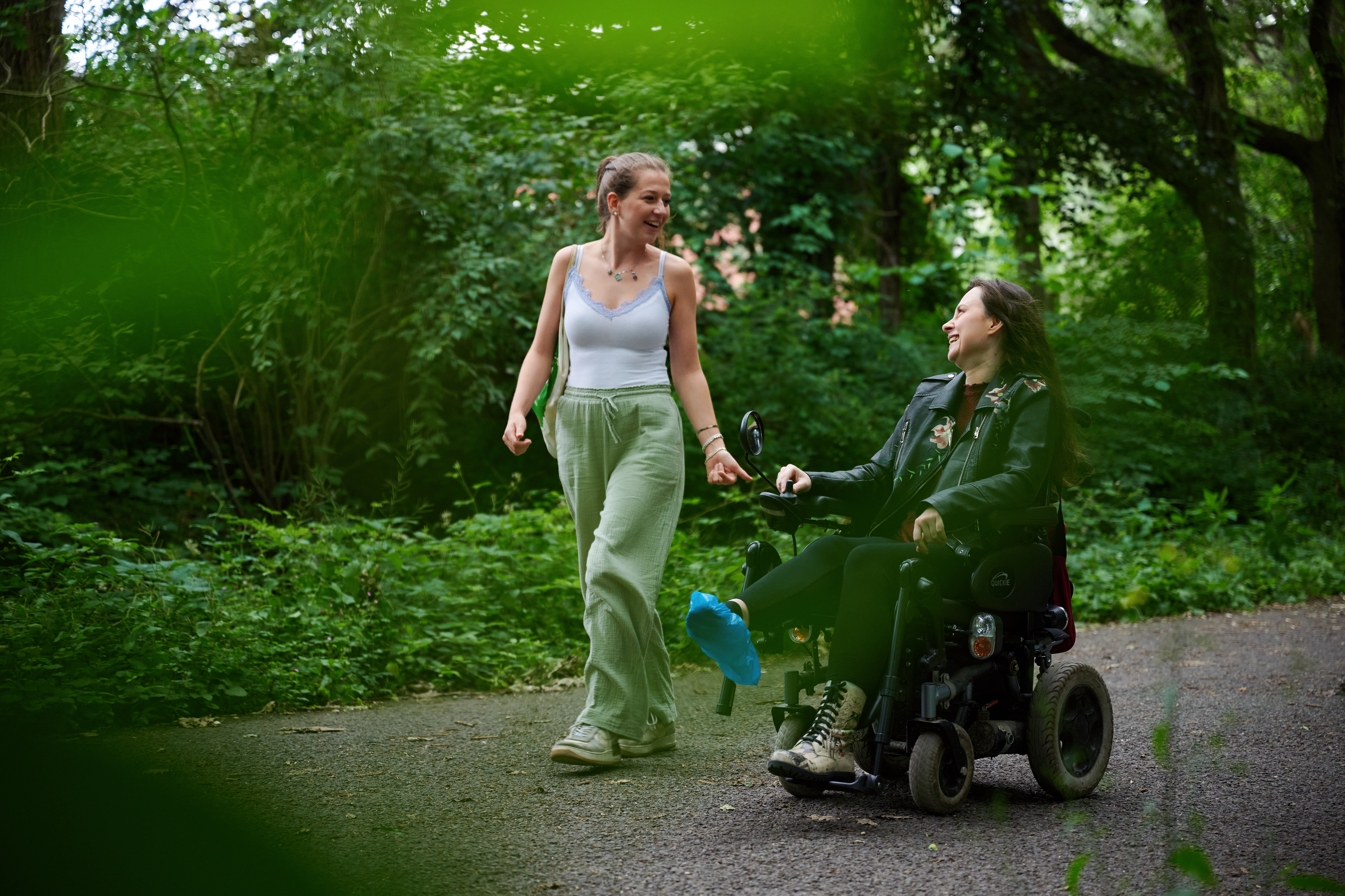 Zwei junge Frauen, eine von ihnen im Rollstuhl lachen bei einem Spaziergang.
