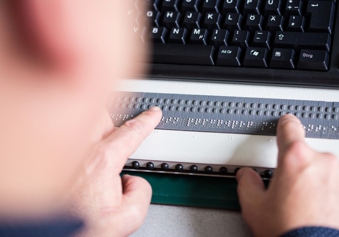 Ein Mensch benutzt eine Tastatur mit Braille-Zeile.