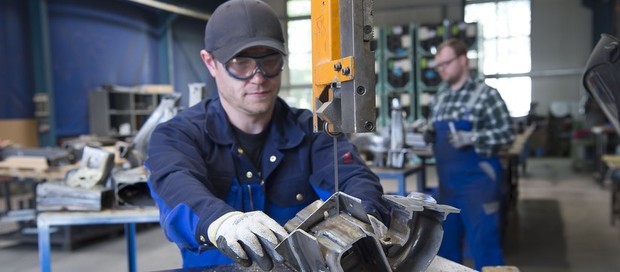 Ein junger Mann arbeitet an einer Metallsäge in einer Werkstatt.